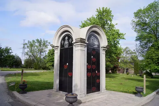 Two ornate black mausoleums in a grassy cemetery under a blue sky