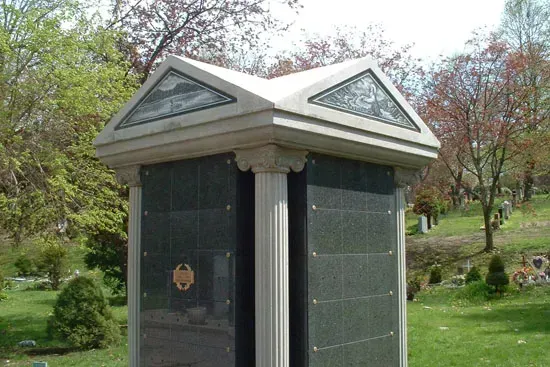 Small stone monument with a triangular roof in a grassy park, surrounded by trees