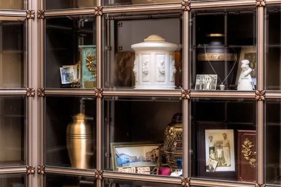Decorative shelf with framed photos, urns, and ornaments in a dark wood display cabinet