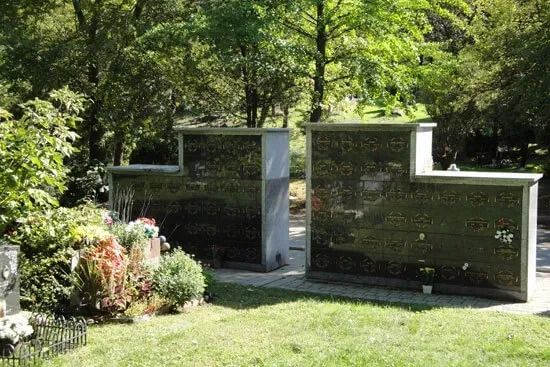 Two modern black memorial headstones in a green cemetery beneath trees