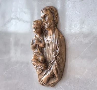 Relief of a bearded man holding a child, mounted on a light stone wall.
