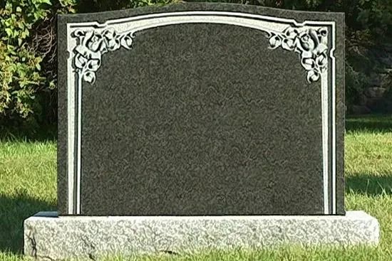 Blank gray gravestone with white decorative corners in a grassy cemetery.