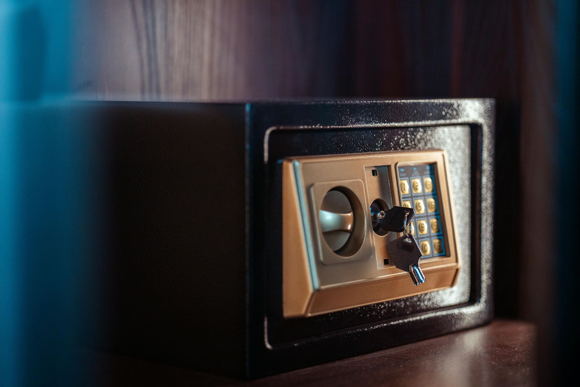 A black electronic safe sits on a wooden surface, with a silver key inserted into the keypad panel.