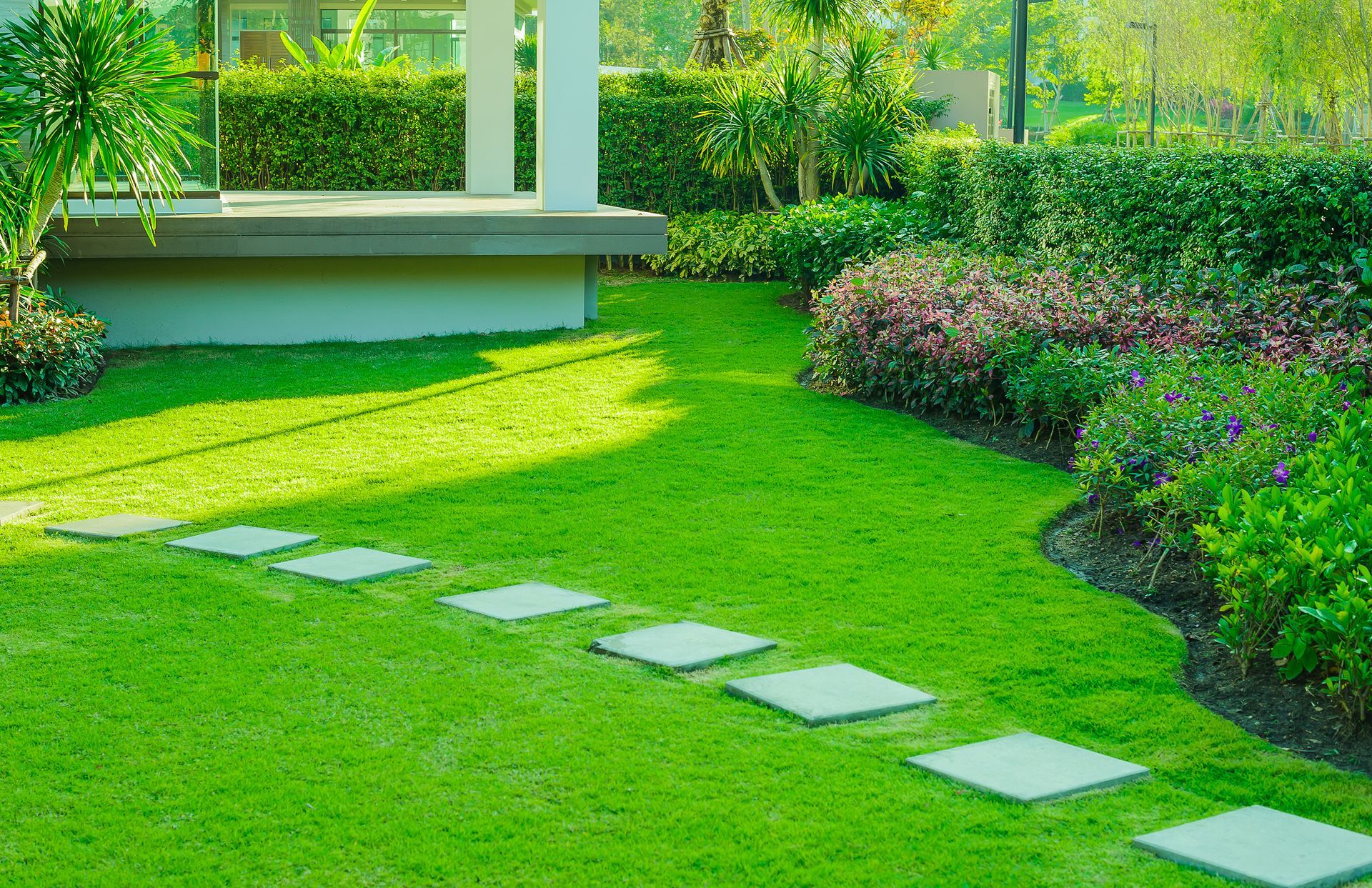 A worker in a high-visibility orange vest mows a green lawn outdoors.