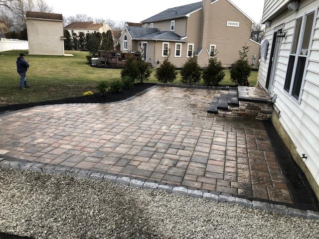 A man is standing in front of a brick patio in front of a house.