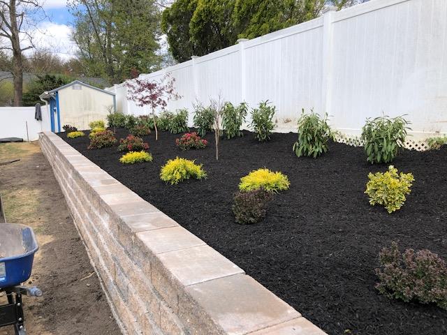 A garden with a brick wall and a white fence surrounding it.