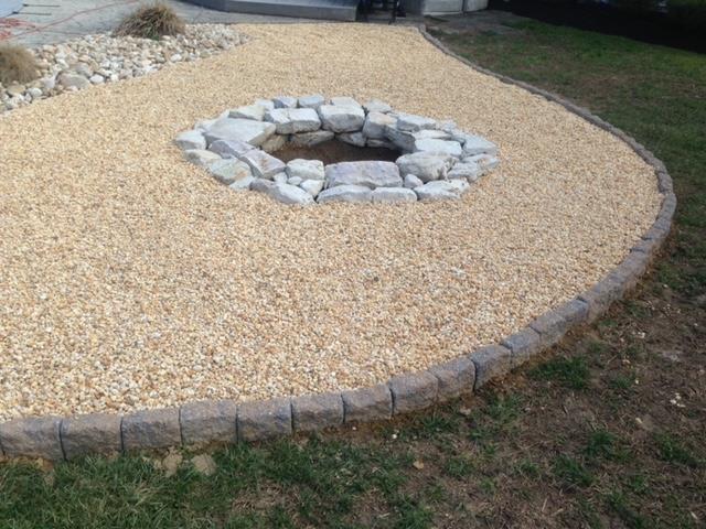 A fire pit is surrounded by gravel and rocks in a yard.