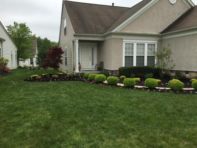 Suburban house with manicured lawn, shrubs, and mulch beds. Cloudy sky.