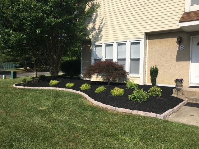 A house with a lush green lawn and a black mulch bed in front of it.