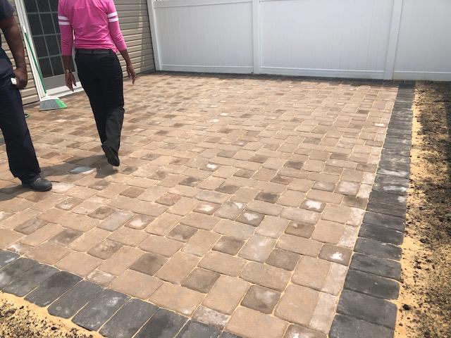 A man and a woman are walking on a brick driveway.