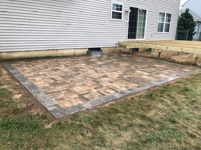 A patio with a wooden deck in the backyard of a house.