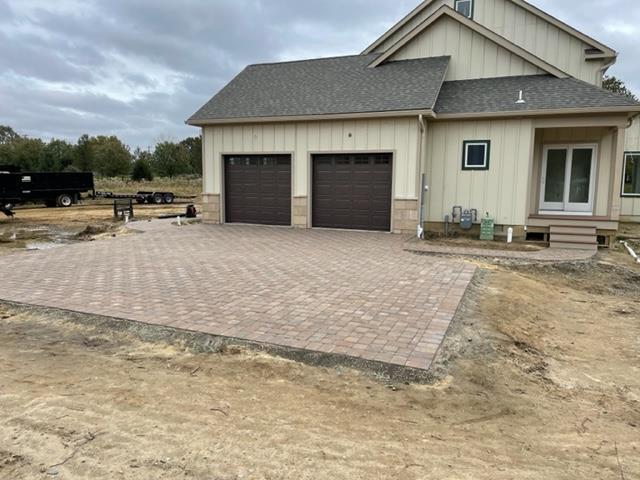 A house with two garage doors and a brick driveway in front of it.