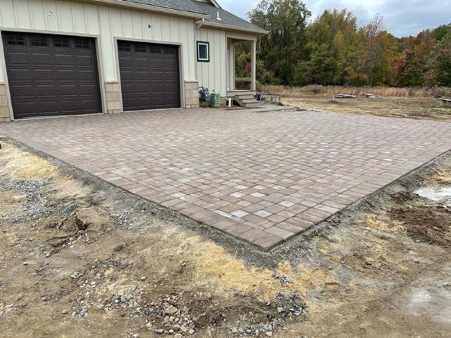 A brick driveway is being built in front of a house with two garage doors.