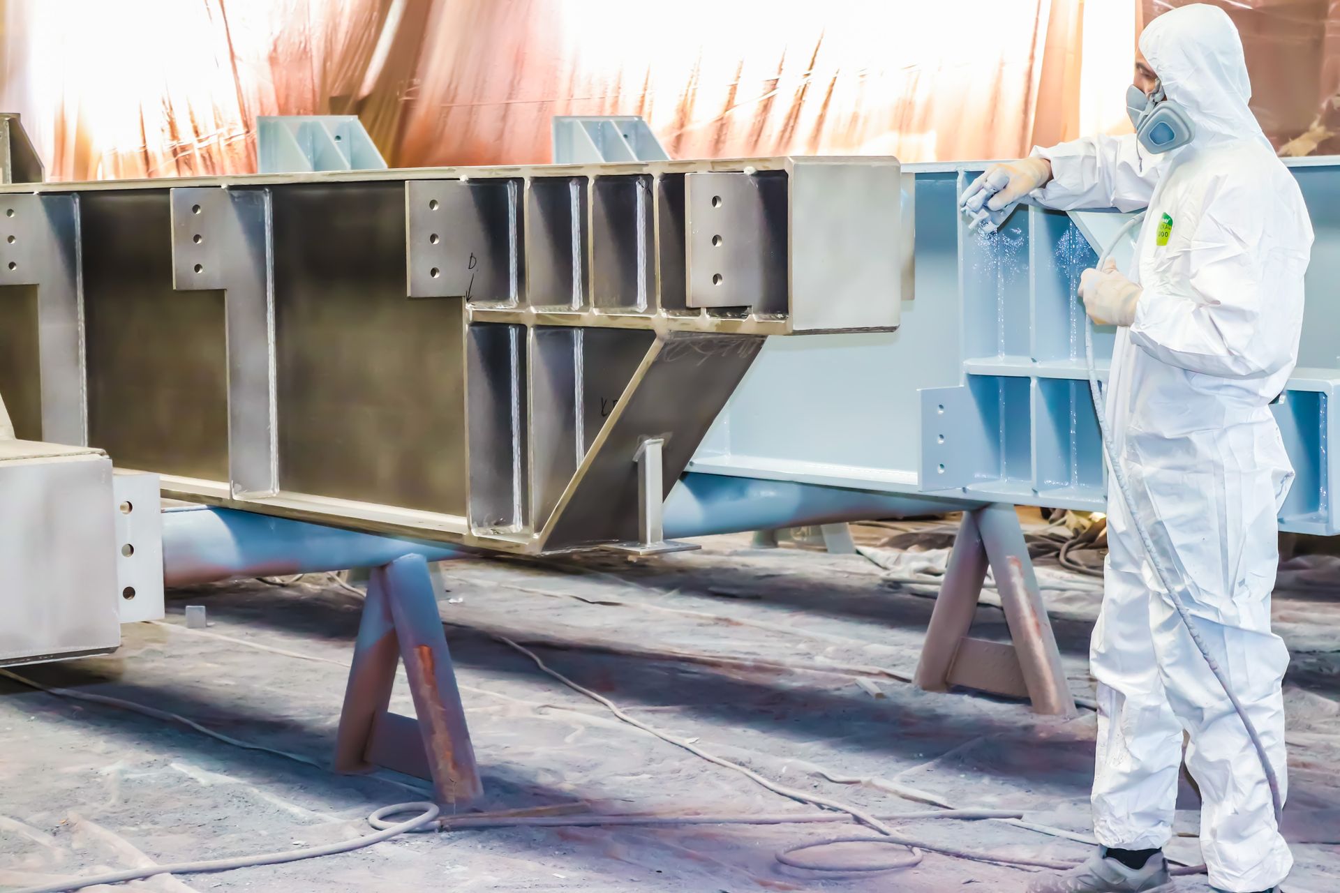 A painter is working to paint a steel structure with a spray gun at an industrial factory.