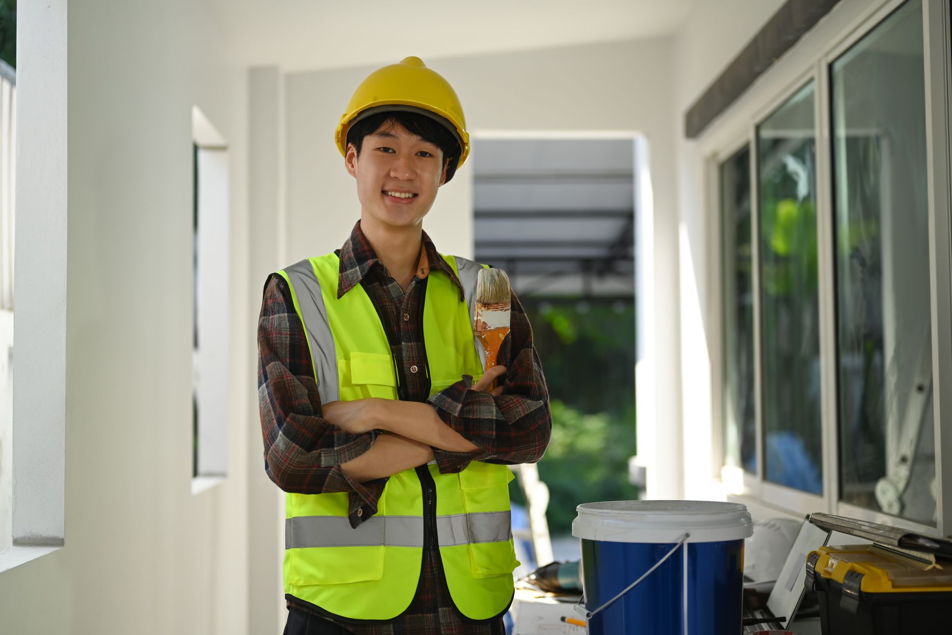 Painter in helmet holding painting brush standing in construction site and smiling at camera.