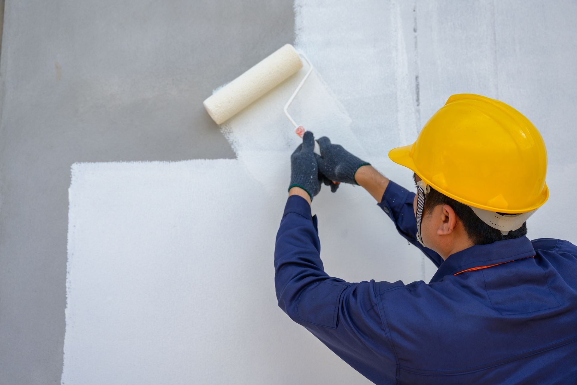 A painter holds a paint roller and skilfully paints the exterior of a commercial space.