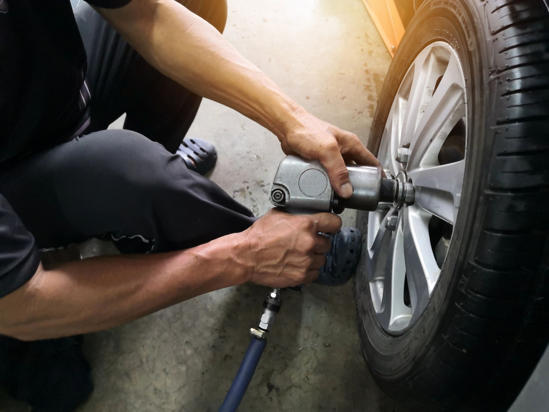 Mechanic using an impact wrench to remove lug nuts from a car tire in a garage.