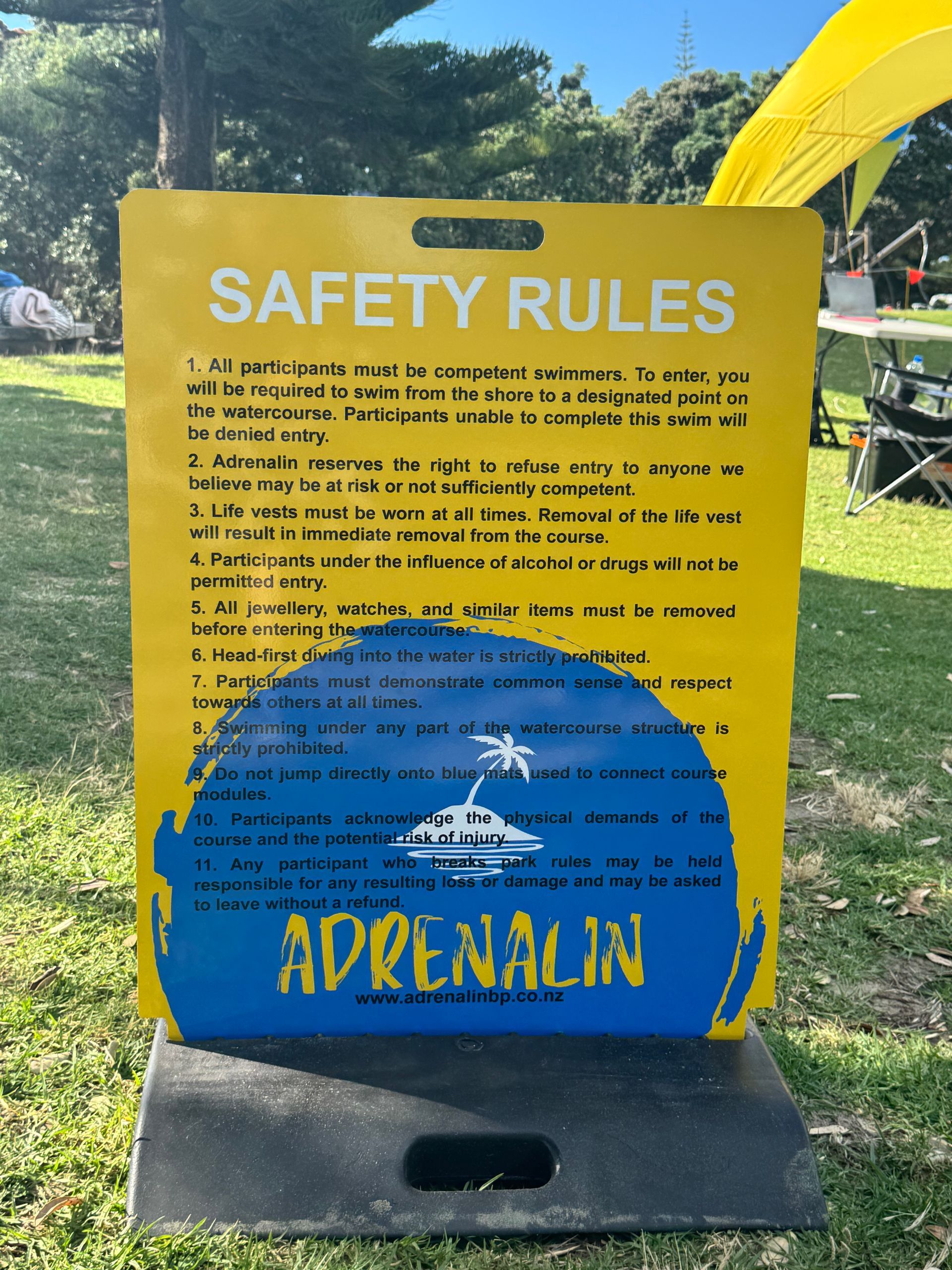 Yellow safety rules sign with blue accents, outdoors, for Adrenalin.