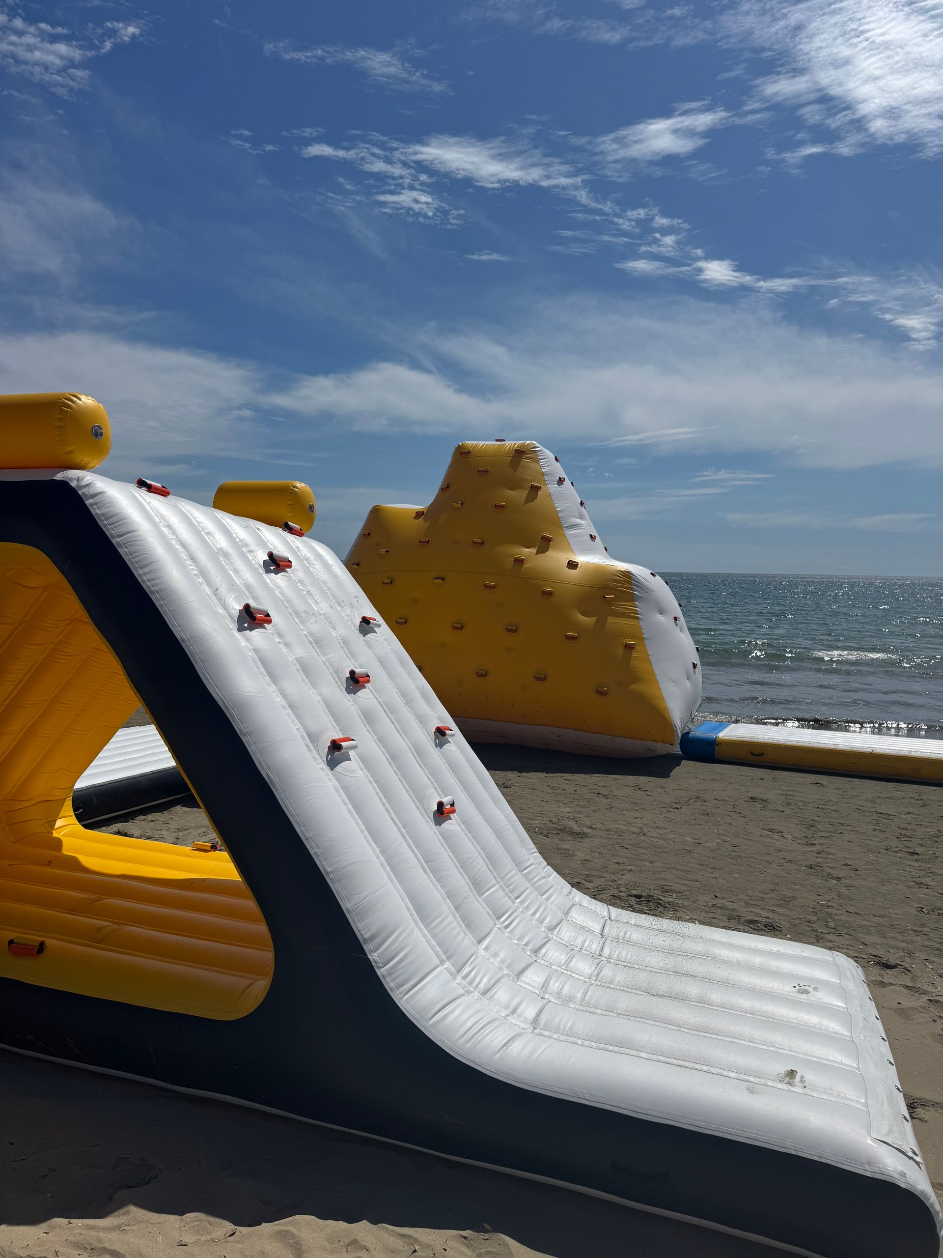 Inflatable climbing structures on a beach, against a blue sky.