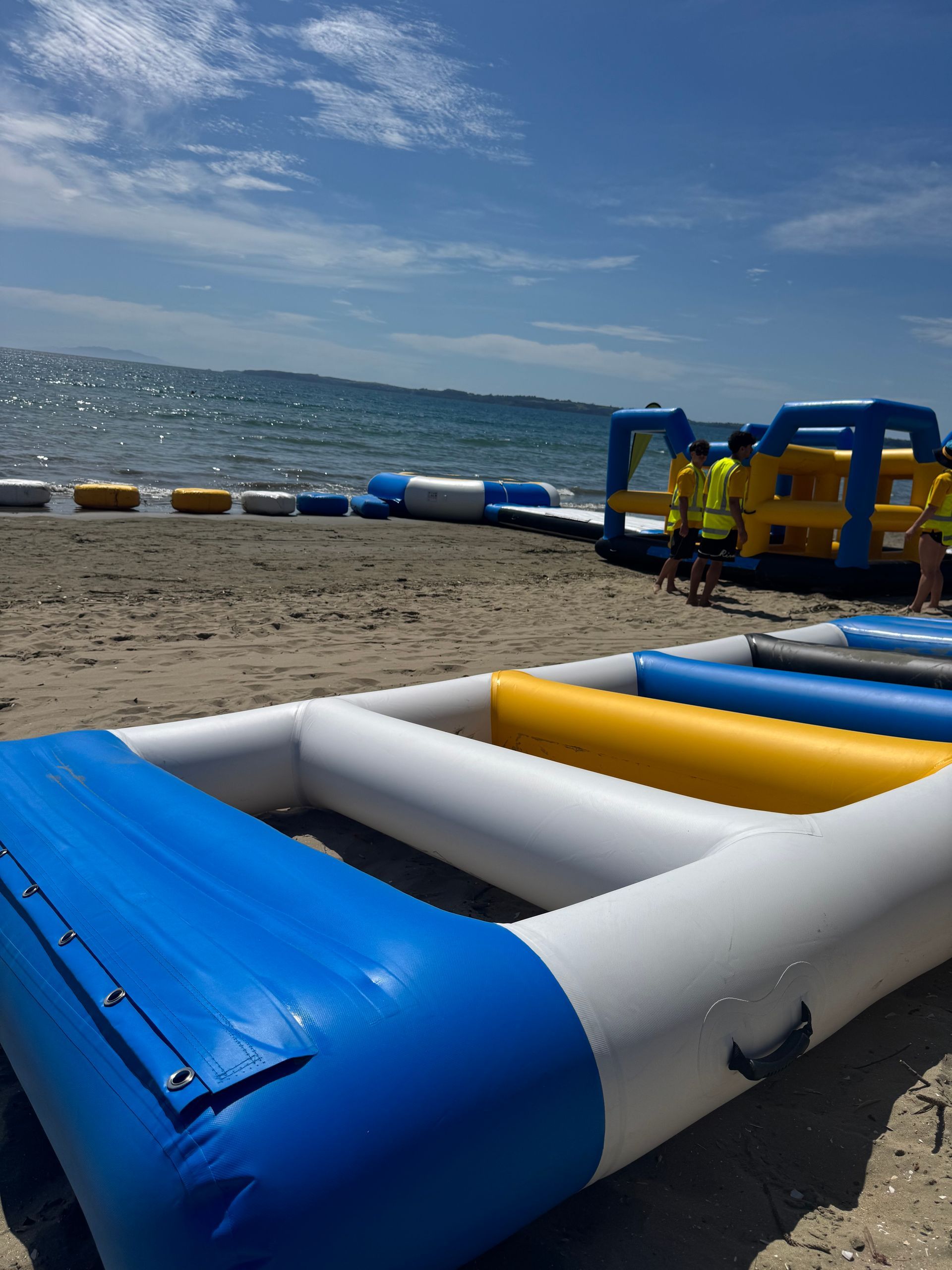 Inflatable water park equipment on a sandy beach, with ocean in the background under a blue sky.