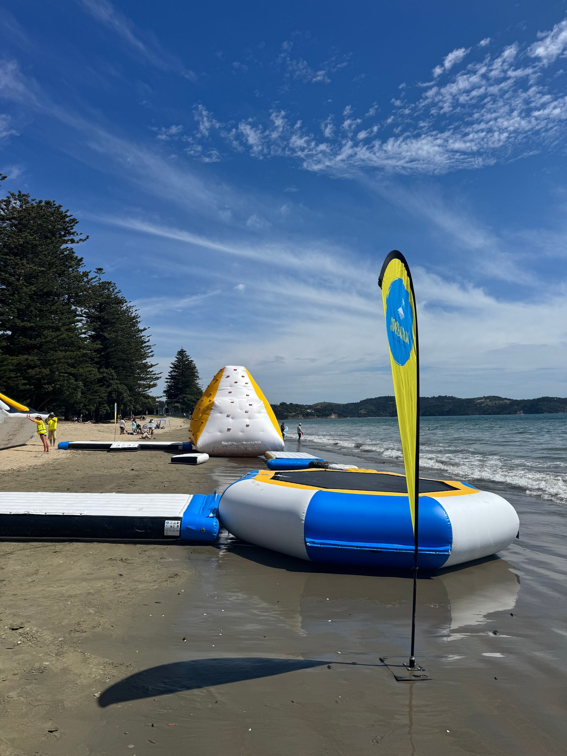 Beach scene with inflatable water park equipment; blue sky, white clouds; yellow and blue structures on sand.