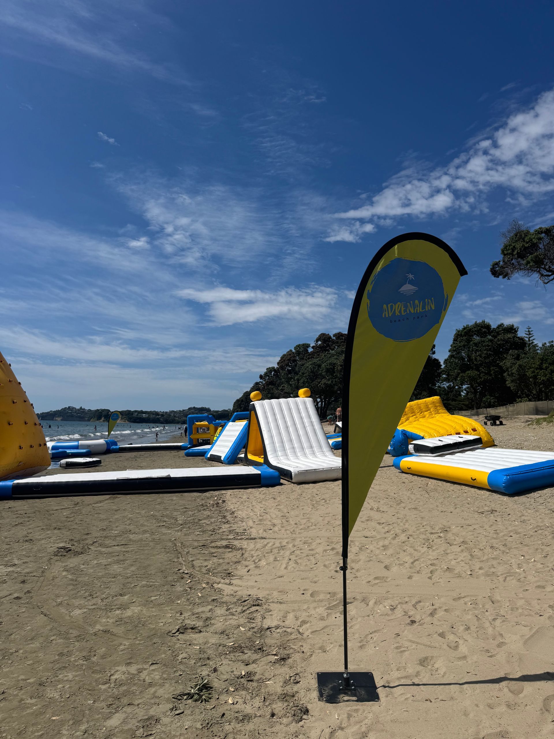 Beach scene with inflatable water park and yellow teardrop flag.