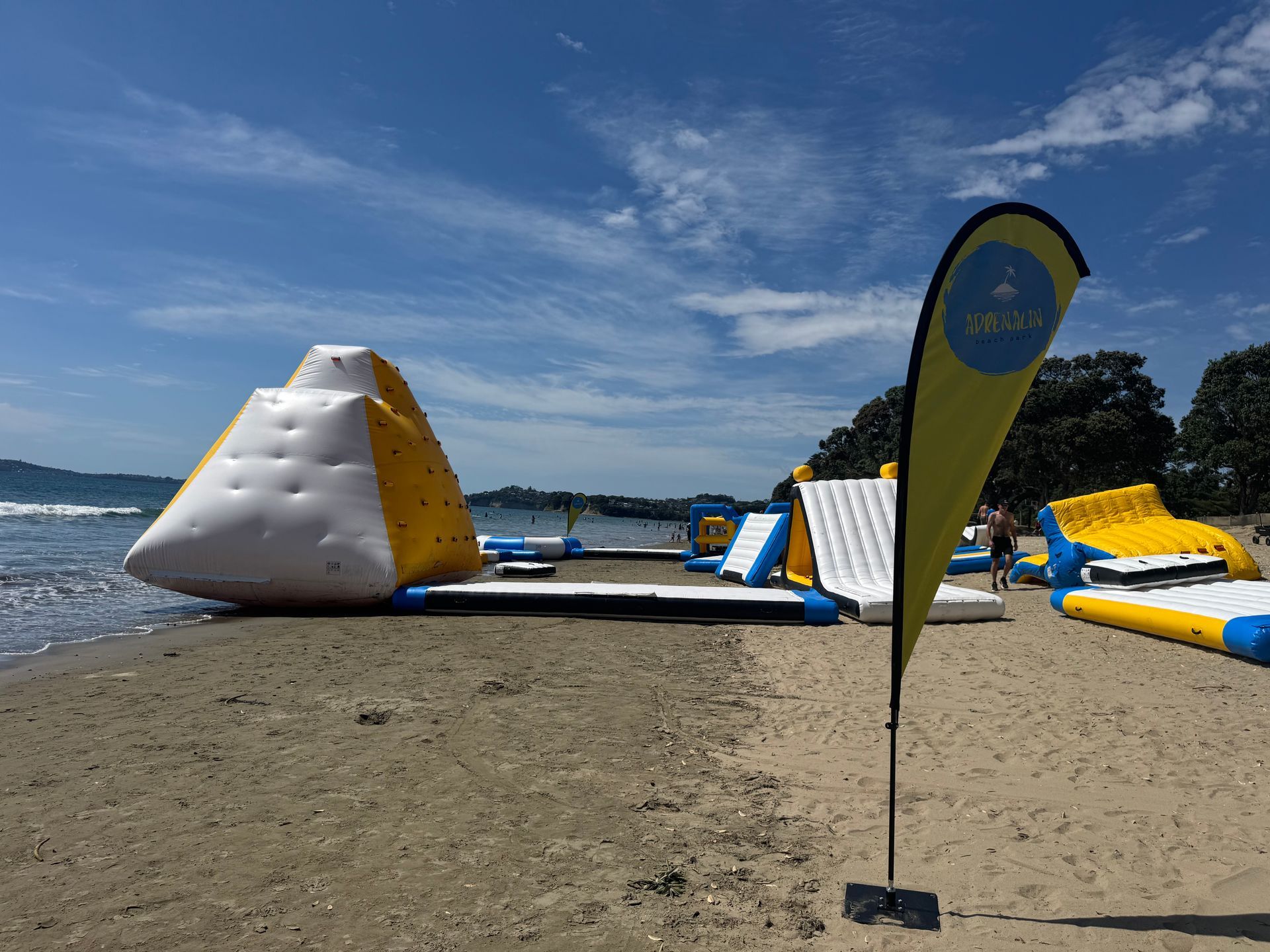 Beach water park with inflatable climbing wall, slides, and obstacle course; sunny day.