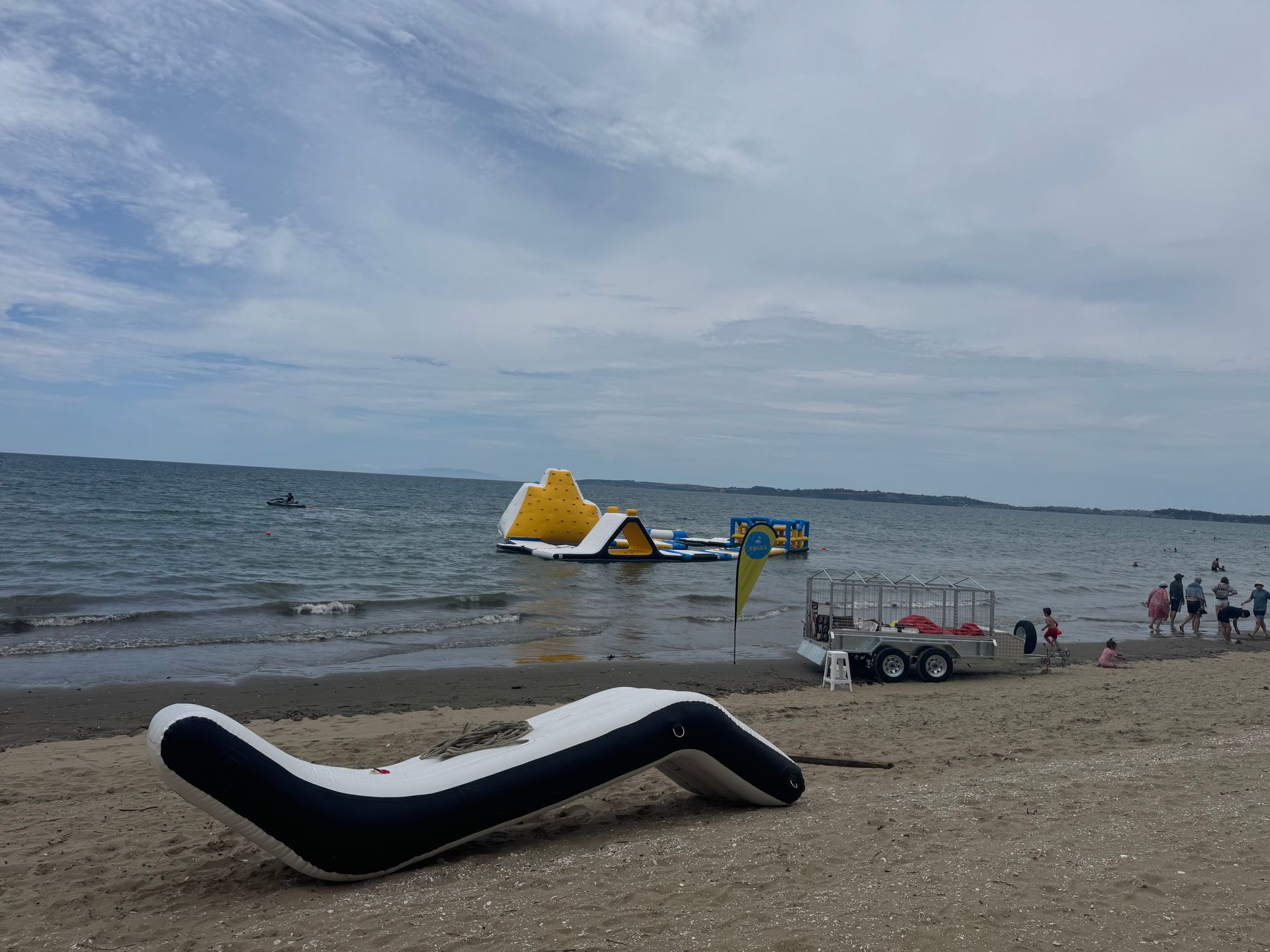 Beach scene with inflatable water park in the sea, people on the shore, and an inflatable lounge chair.