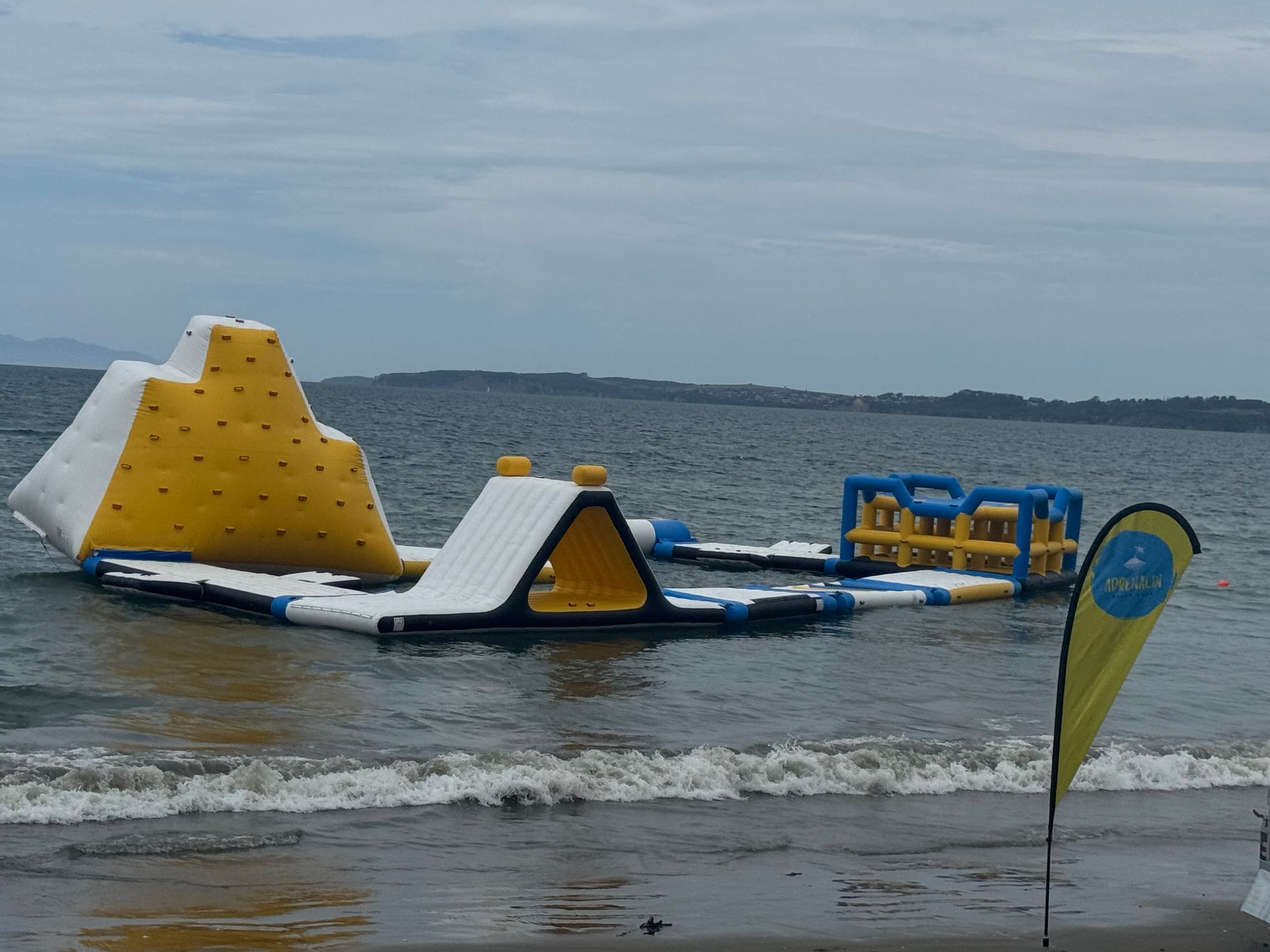 An inflatable water park on a body of water with a yellow climbing wall and other obstacles.