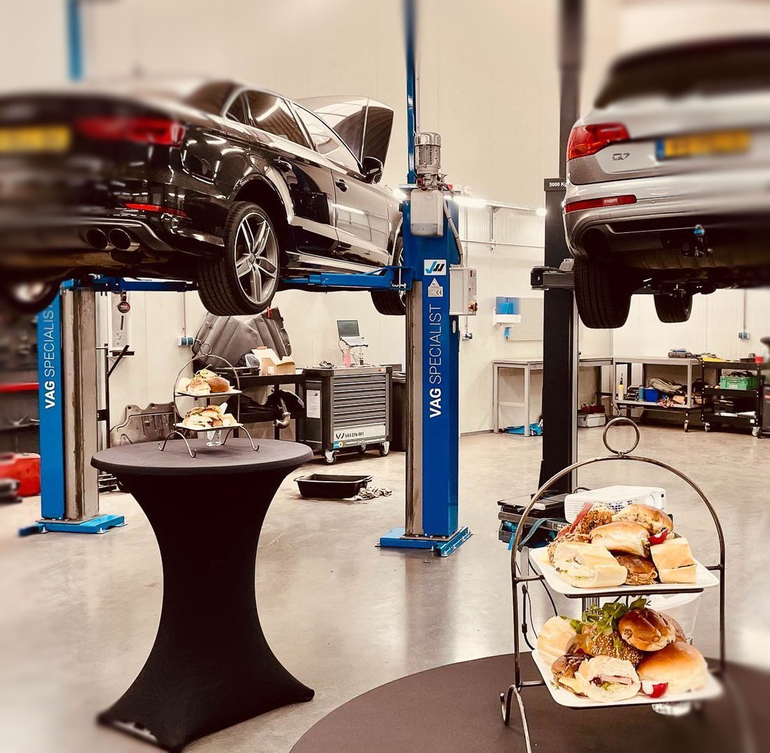 Een auto staat op een lift in een garage naast een tafel met eten erop.