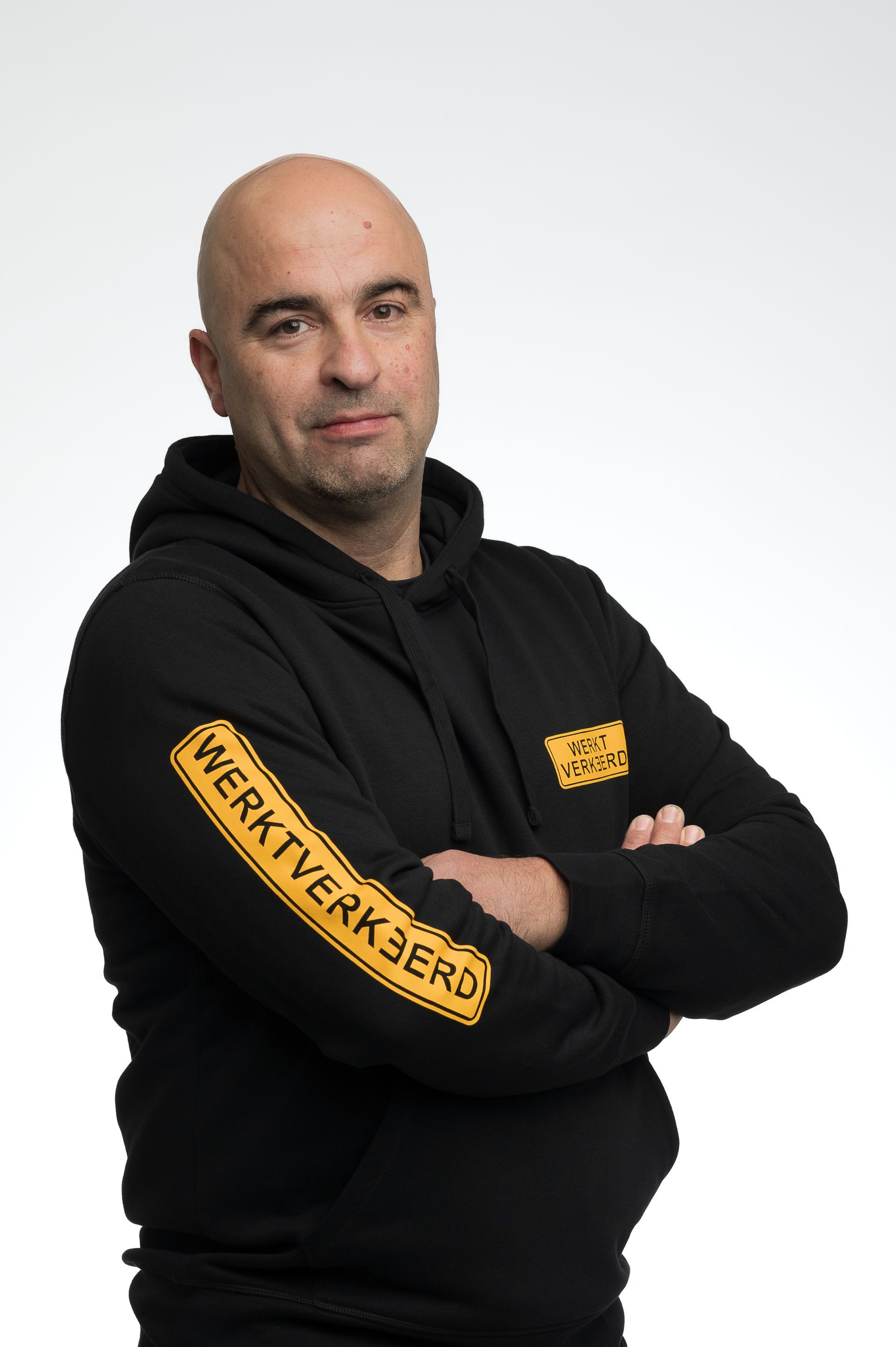 Vijf lachende vrouwen poseren samen binnenshuis, met kleding in verschillende kleuren, bij een raam.