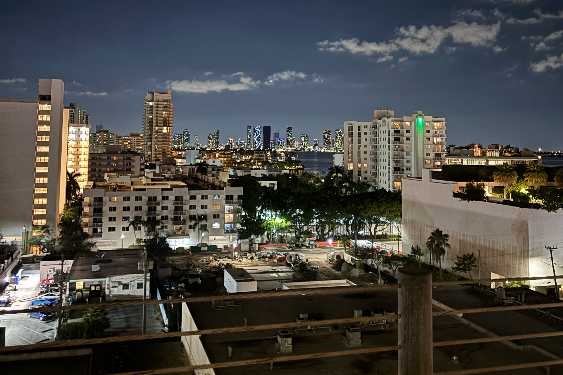 A night view of a cityscape featuring apartment buildings, street lighting, and distant skyscrapers under a dark sky.