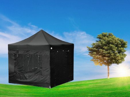 A black tent is sitting on top of a lush green field next to a tree.