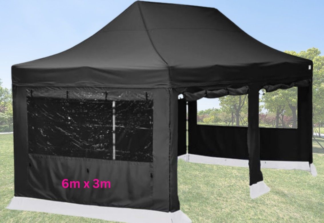 A black tent is sitting on top of a lush green field next to a tree.