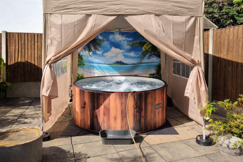 A wooden hot tub with steps in a backyard with a palm tree in the background.