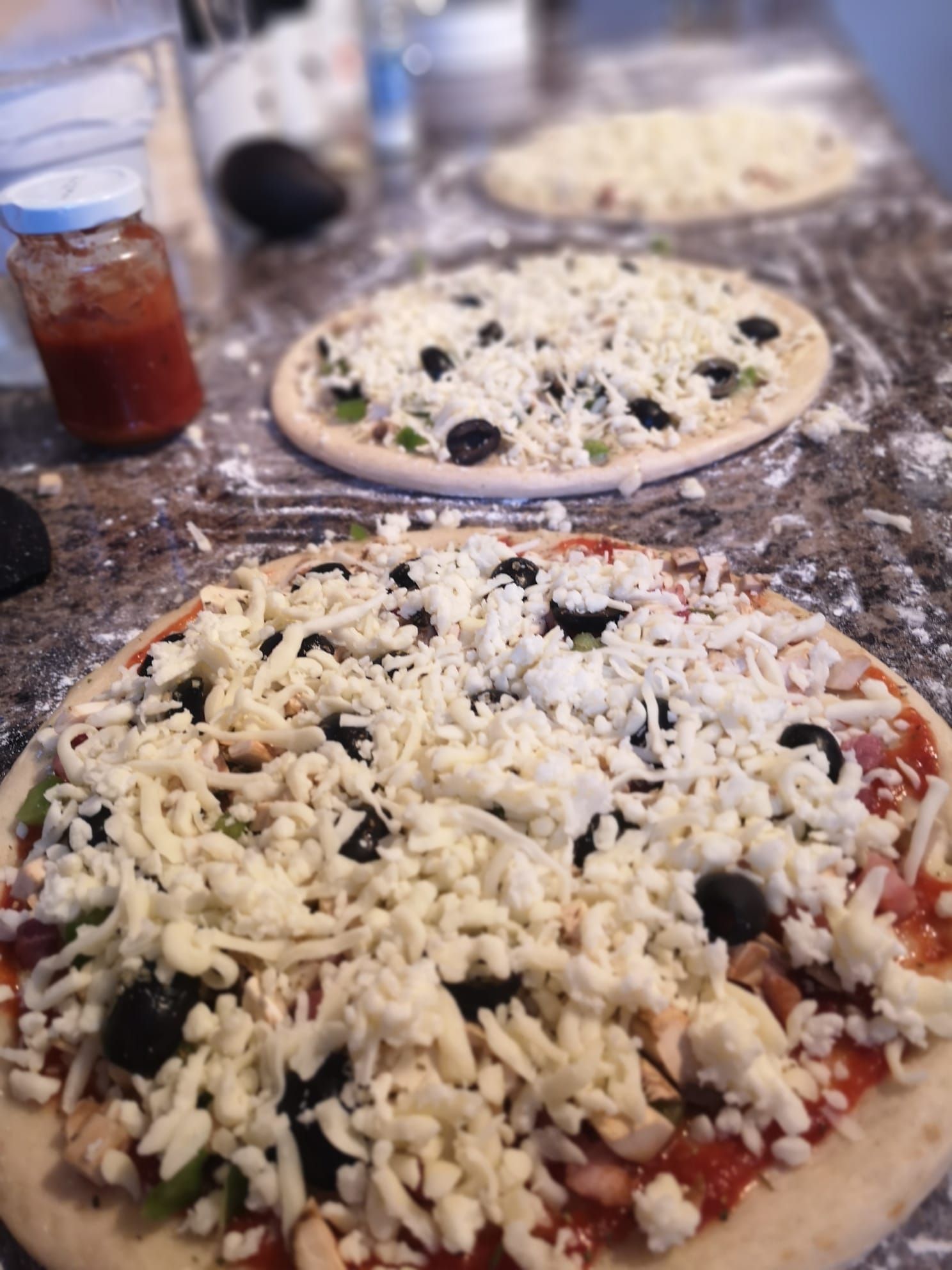 Three pizzas are sitting on a counter covered in cheese.