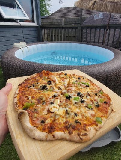 A person is holding a pizza on a cutting board in front of a hot tub.
