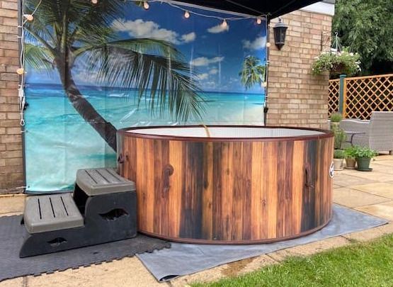 A wooden hot tub is sitting under a canopy in a backyard.