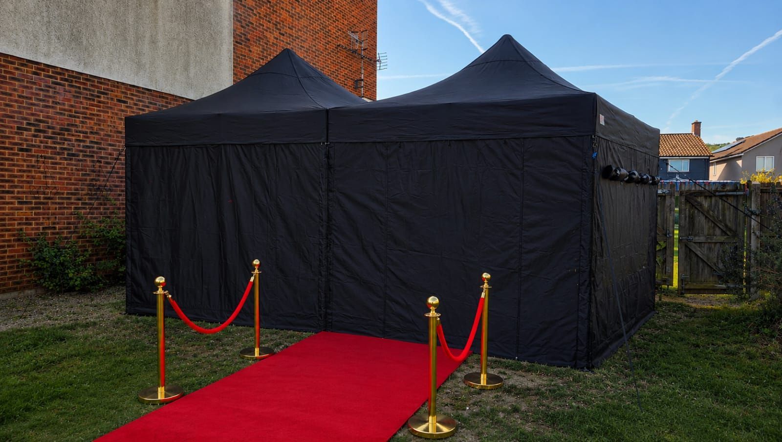 Black marquee tent on a lawn with a red carpet entrance and stanchions