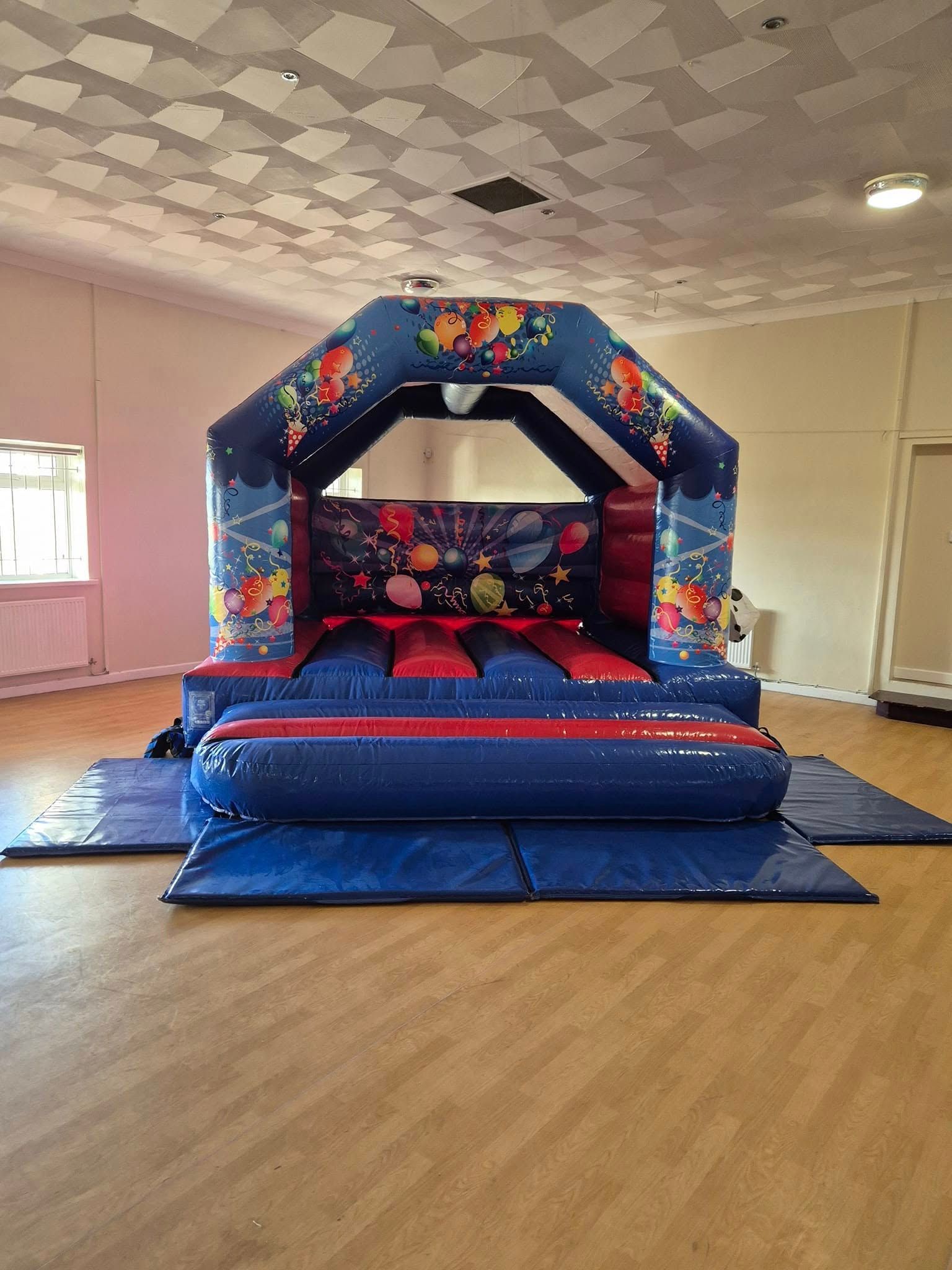 A blue and red bouncy castle is sitting on top of a blue mat in a room.