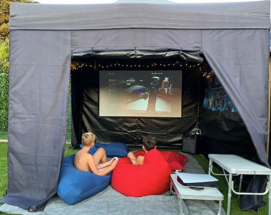 A group of people are sitting under a tent watching a movie