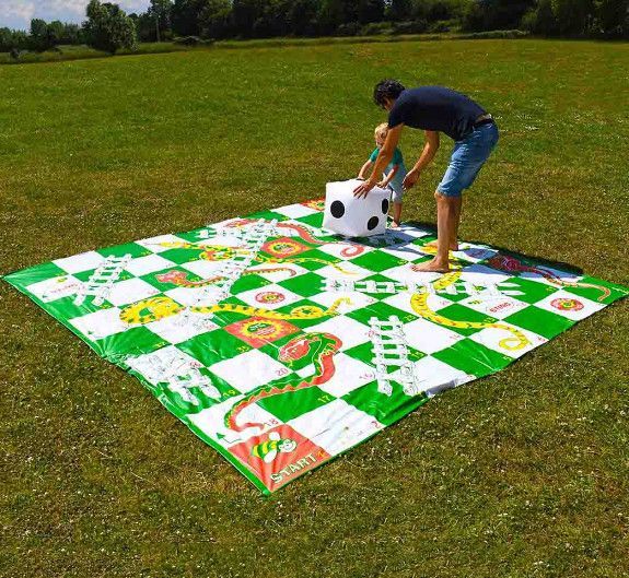 A man and a child are playing a giant snakes and ladders game.