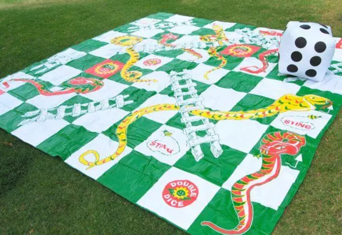 A man is playing a giant snakes and ladders game with a child.