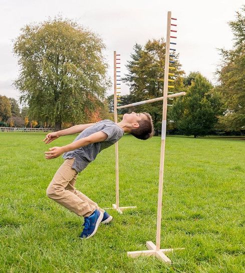 A young boy is jumping over a wooden pole in a field.