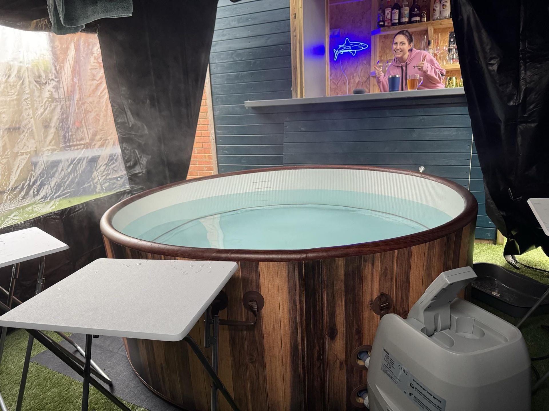 A wooden hot tub is sitting next to a white table.