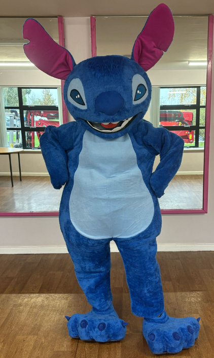 A person in a stitch mascot costume is standing in a room with their hands on their hips.