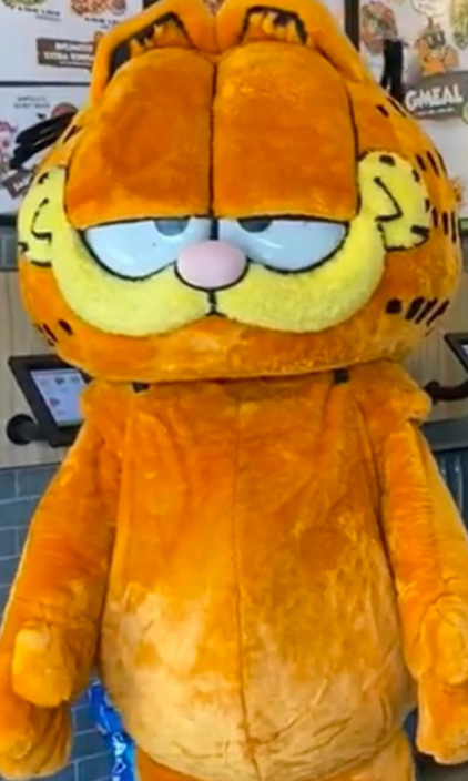 A stuffed garfield mascot is standing in a restaurant.
