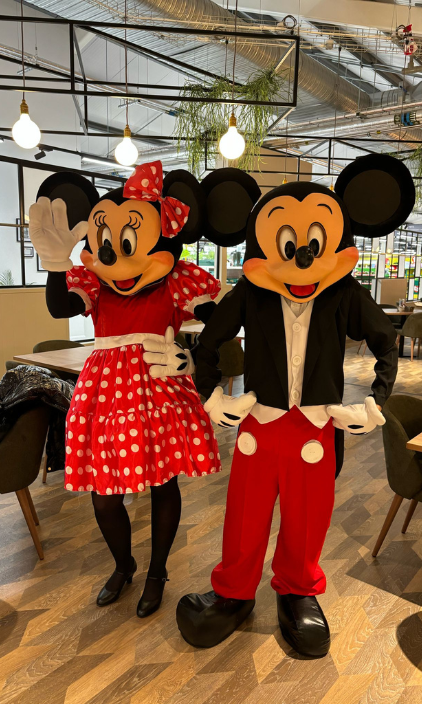 Mickey mouse and minnie mouse mascots are standing next to each other in a restaurant.