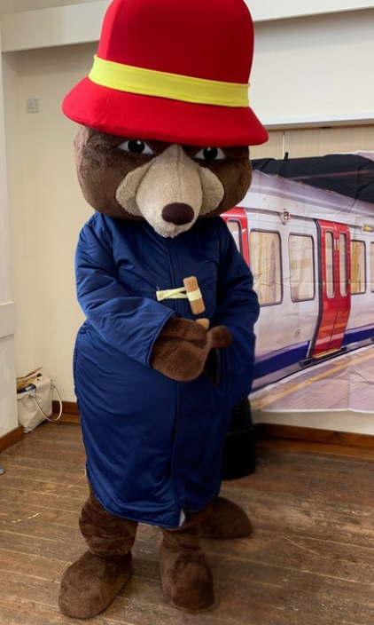 A mascot bear wearing a red hat is standing in front of a train