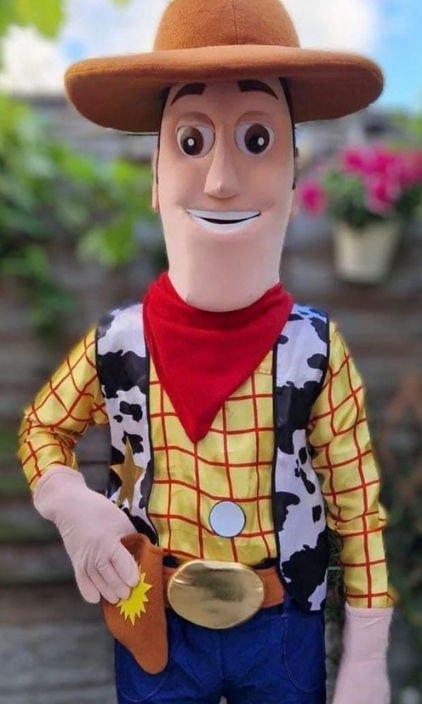A mascot dressed as woody from toy story is standing in front of a wooden fence.